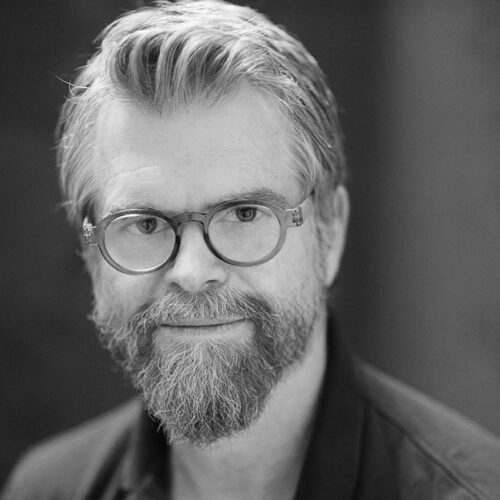 Black-and-white headshot of Scott Hamilton Kennedy, Academy Award-nominated documentary filmmaker, wearing glasses and looking directly at the camera.