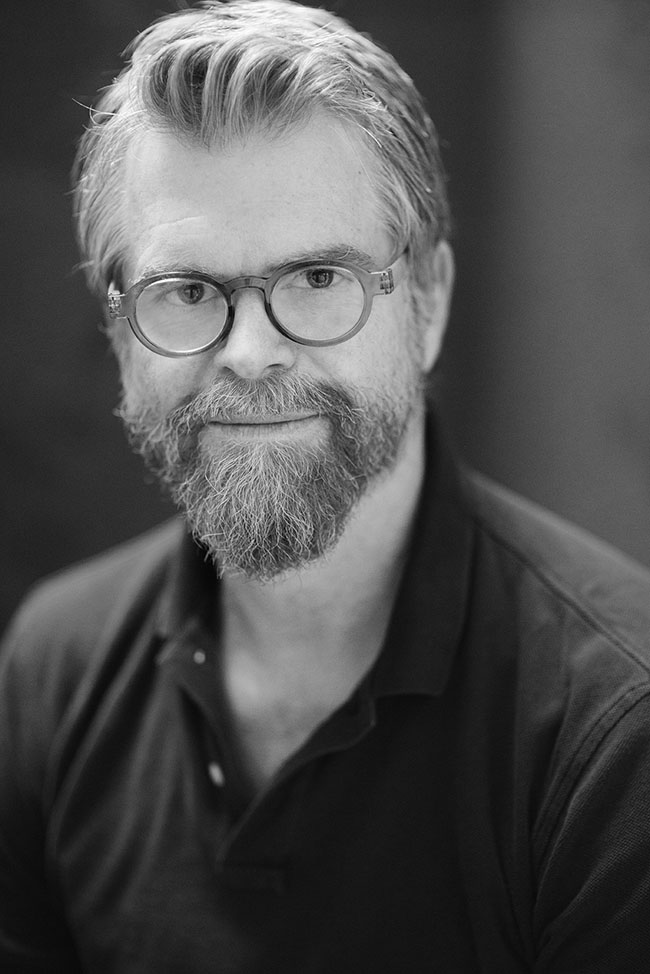 Black-and-white headshot of Scott Hamilton Kennedy, Academy Award-nominated documentary filmmaker, wearing glasses and looking directly at the camera.